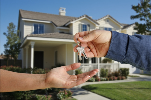 house in background and two hands exchanging keys in foreground